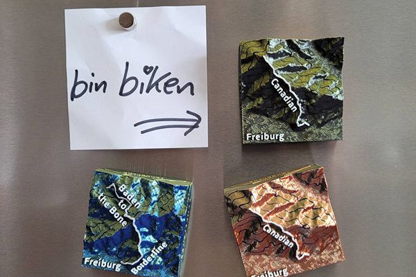 Mehrere verschiedenfarbige MTB-Trail Dekomagnete und Notizzettel "bon biken" an Kühlschrank