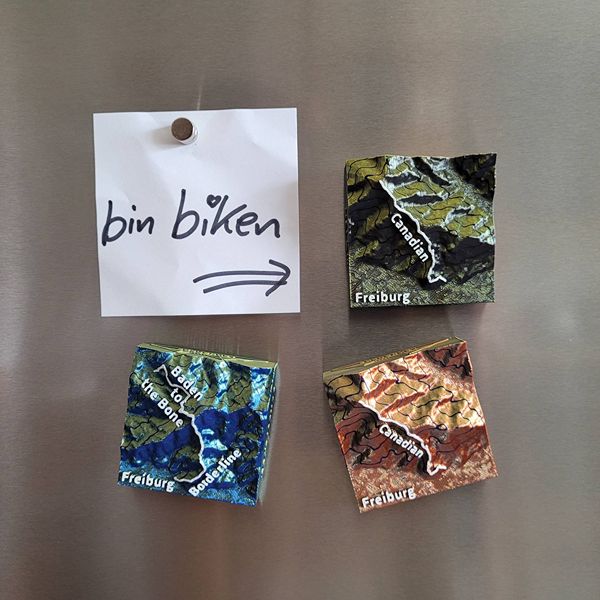 Mehrere verschiedenfarbige MTB-Trail Dekomagnete und Notizzettel "bon biken" an Kühlschrank